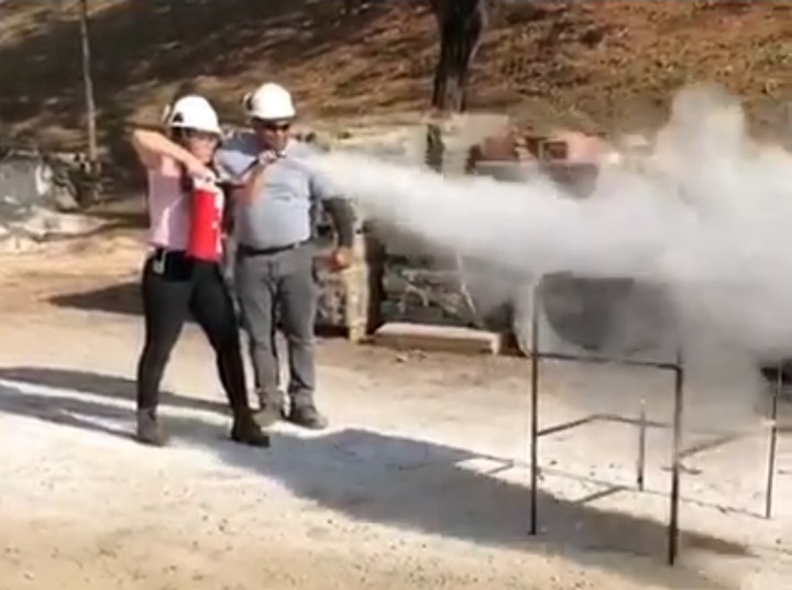 Treinamento prático de combate a incêndio com extintor, capacetes e simulação em ambiente externo.